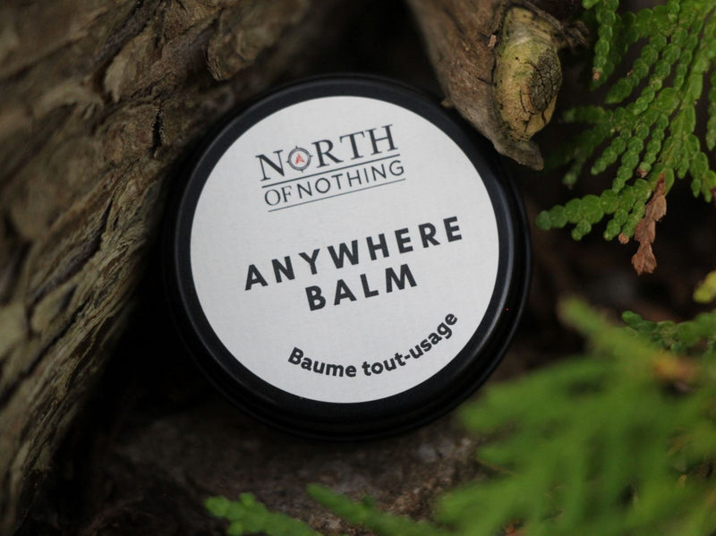 North of Nothing Anywhere Balm displayed outdoors among cedar branches and natural wood. 